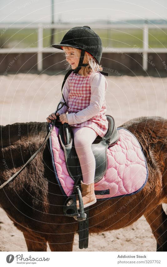 Kleines glückliches Mädchen reitet Pferd auf dem Hippodrom Lächeln Sport Mitfahrgelegenheit Porträt Reiterin Kind üben Kindheit wenig Jockey ländlich Glück Tier