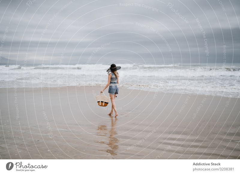 Junge Frau geht barfuss am Sandstrand Hut Strand Tasche modisch glamourös Meer Sommer Urlaub reisen Erholung Feiertag Landschaft malerisch jung Person attraktiv