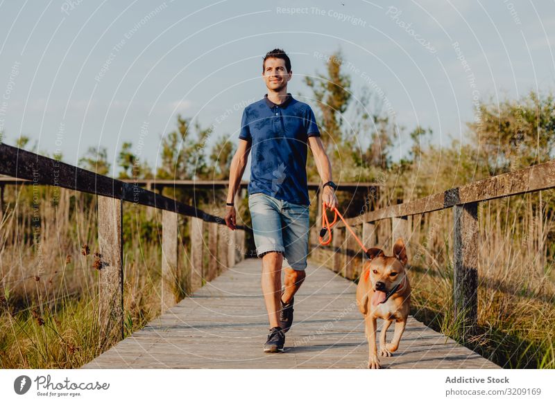 Glücklicher erwachsener Mann geht mit Hund durch die Landschaft laufen lässig heiter anleinen braun ländlich hölzern Baum Grün Tageslicht Haustier Zusammensein