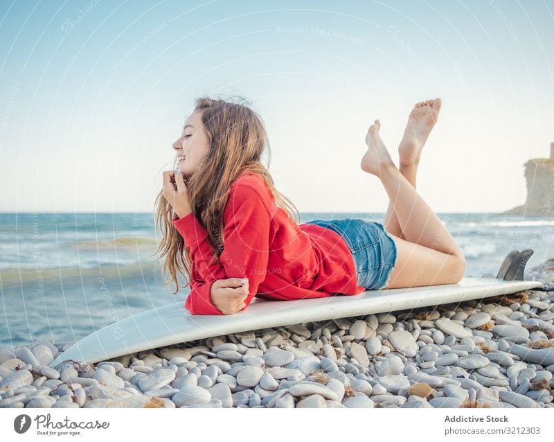 Fröhliche Frau mit gekreuzten Beinen auf einem Surfbrett liegend Erholung Lächeln Meer Lügen Feiertag hübsch Sport Strand heiter schön Glück attraktiv Urlaub