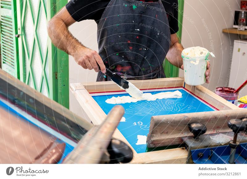 Männlicher Künstler erstellt Druck auf T-Shirt Meister Bildschirm drucken Siebdruck Serigraphie erschaffend Werkstatt Hobby Staffelei dreckig Schürze Stil Farbe