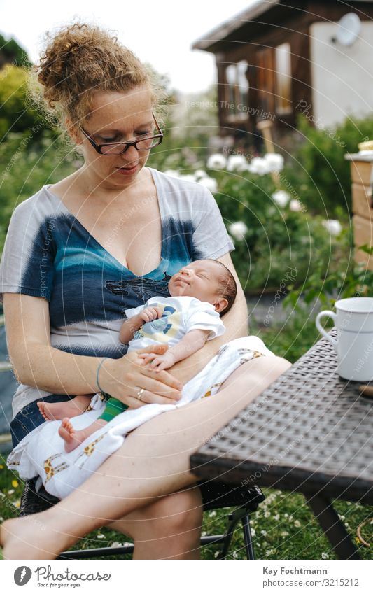 kaukasische Mutter mit ihrem Neugeborenen, die draußen in ihrem Garten sitzt Zuneigung Baby schön blond Bonden Pflege Kaukasier Stuhl Kind Kindheit niedlich