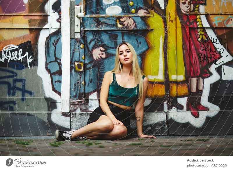 Stilvolle Frau mit Sonnenbrille posiert an Graffiti-Wand auf Stadtstraße. stylisch Straße urban posierend Sitzen Porträt attraktiv Schönheit trendy Lifestyle