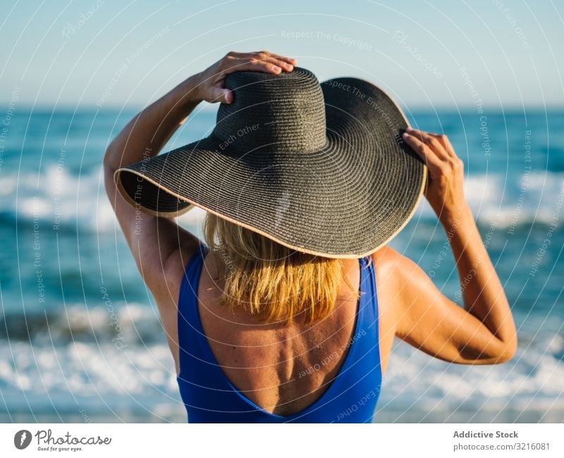 Frau in blauem Badeanzug und Hut am Sandstrand schlank Strand schäumen sandig Badebekleidung winken Wasser Sommer Freizeit Bräune attraktiv Seeküste bedeckt
