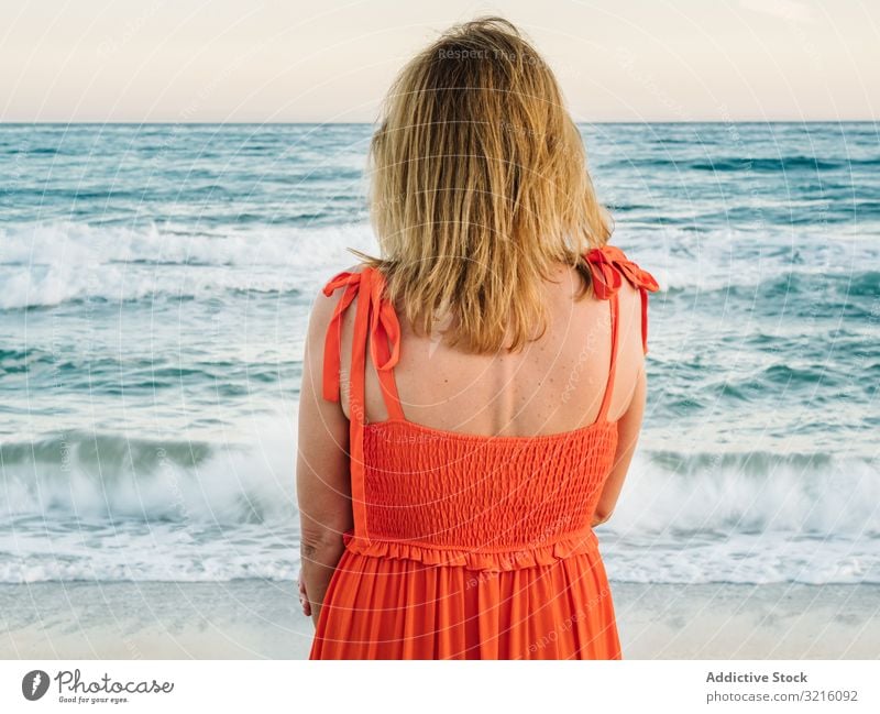 Frau in rotem Kleid schaut am Meer entlang Strand sandig Wasser Wellen nachdenklich genießend Sommer entspannend Freizeit Meereslandschaft Lifestyle Urlaub