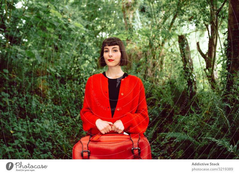 Frau in Rot mit großem roten Koffer im Wald reisen stylisch grün Gepäck Natur schön Tasche Piercing Warten Freiheit allein Ausflug Reise Buchse Baum Tourist