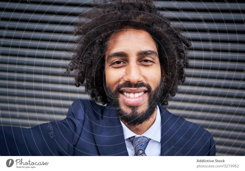 Fröhlicher ethnischer Mann, der Egoismus nimmt und lächelt modern Geschäftsmann formal Afrikanisch schwarz Smartphone Selfie Wand Lächeln Glück Afro-Look heiter