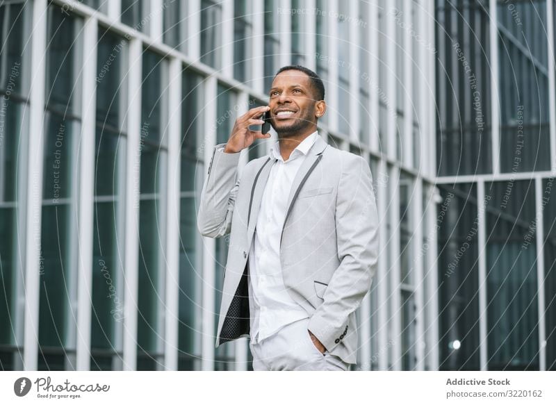 Eleganter schwarzer Mann mit Smartphone in Gebäudenähe laufen sprechend Business Architektur Anzug professionell ethnisch Außenseite Afrikanisch Surfen