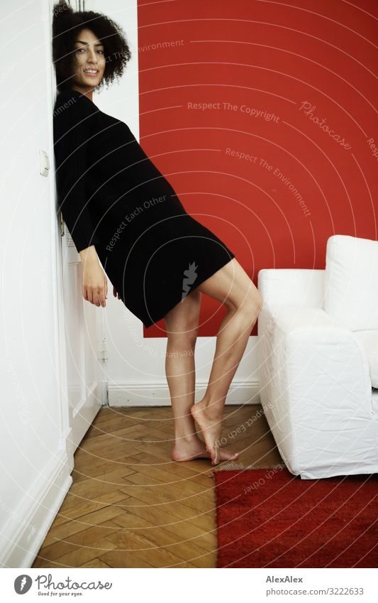 Portrait einer Jungen Frau vor roter Wand Stil Freude schön Wohlgefühl Wohnung Sessel Wohnzimmer Junge Frau Jugendliche Beine 18-30 Jahre Erwachsene Pullover
