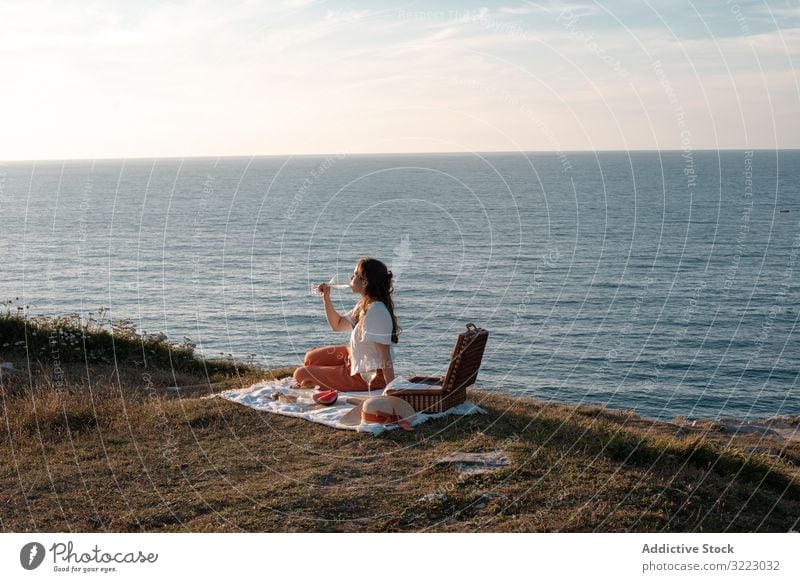 Frau mit Glas Getränk auf Picknickmatte mit Blick auf Meer und Berge Seeküste Strand Sommer lesen Freizeit Himmel MEER sich[Akk] entspannen trinken Urlaub