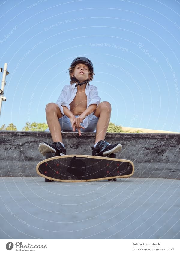 Junge mit Skateboard auf Rampe sitzend Skatepark Schutzhelm Lifestyle Holzplatte Sitzen Sport Freizeit Hobby männlich jung Kindheit Sommer sonnig vorsichtig