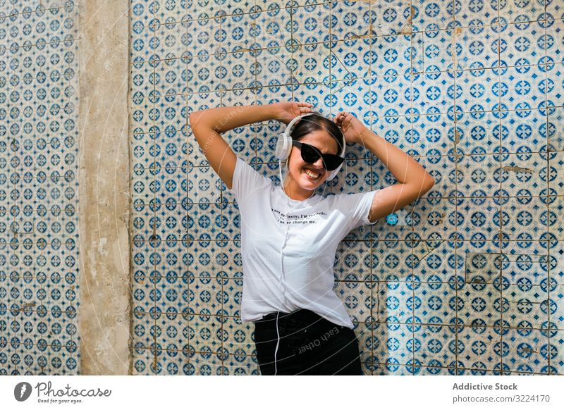 Fröhliche, ungezwungene Frau mit Sonnenbrille steht auf Stadtstraße Kopfhörer stylisch heiter trendy tausendjährig schön Apparatur Musik Gerät Glück Gebäude