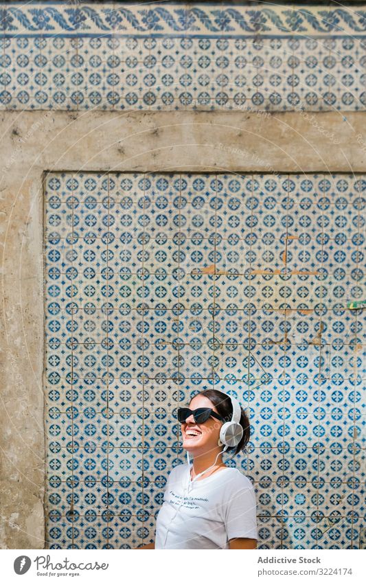 Fröhliche, ungezwungene Frau mit Sonnenbrille steht auf Stadtstraße Kopfhörer stylisch heiter trendy tausendjährig schön Apparatur Musik Gerät Glück Gebäude