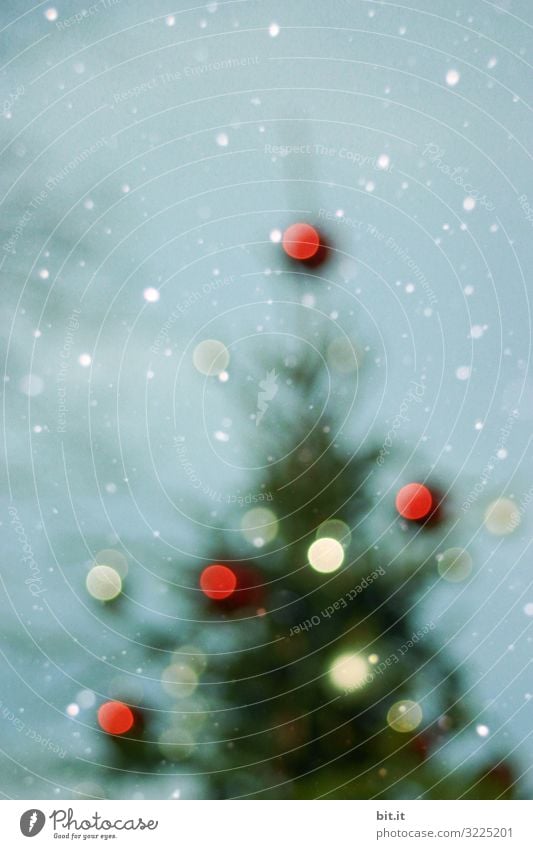 Unscharf l unscharfer Weihnachtsbaum mit verschwommenen Lichtpunkten im Schneefall vor blauem Himmel. Christbaum mit unscharfen vielen Christbaumkugeln in rot und weiß im Schnee. Weihnachten im Schnee, mit leuchtenden Kugeln als Dekoration, Verzierung.