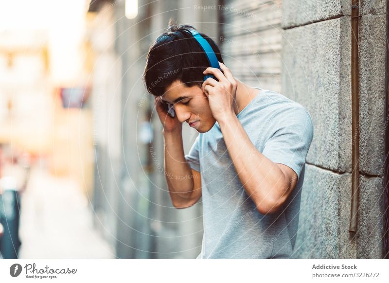 Mann mit Kopfhörern, der auf der Straße Musik hört Großstadt zuhören benutzend Streaming Inhalt cool freudig modern lässig stehen sonnig Stadt jung Erwachsener