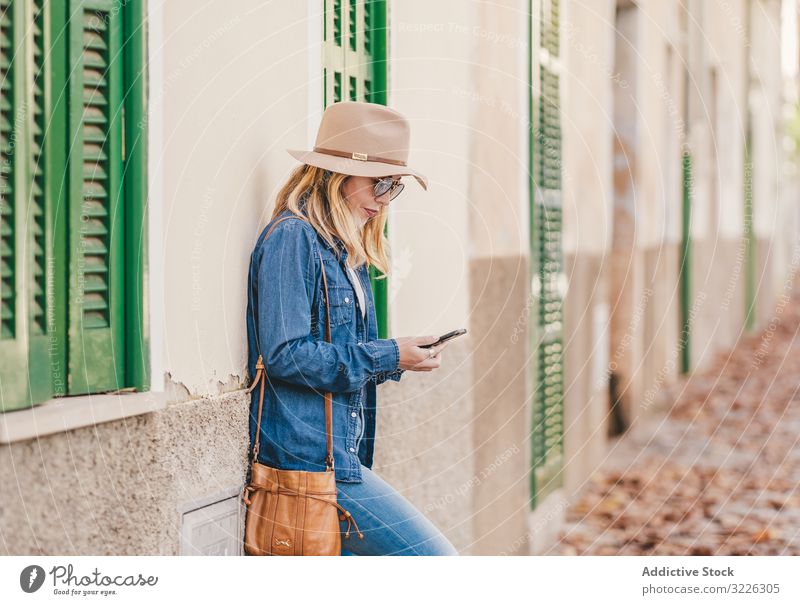 Frau mit Smartphone lehnt an Steinhaus Glück schön sprechend attraktiv charmant Erholung Straße selbstbewusst Model Mitteilung nachdenklich Lächeln lieblich