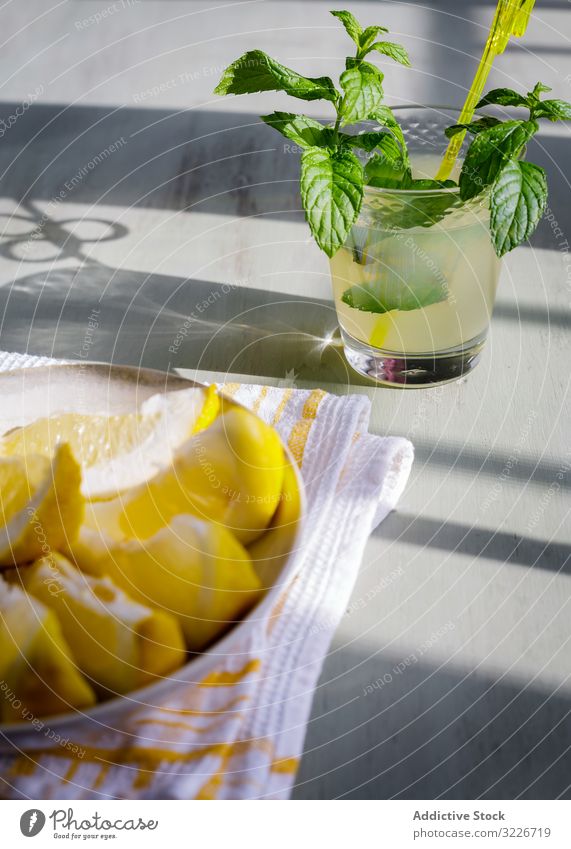 Glas frische Limonade neben dem Teller mit geschnittenen Zitronen auf dem Tisch Spielfigur Saft Küche hölzern rustikal selbstgemacht Minze Frucht trinken