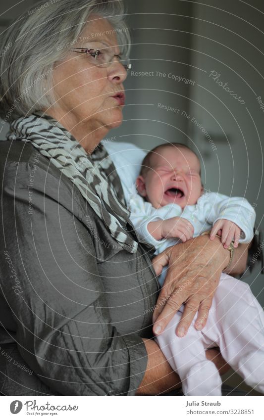 Schicke Oma mit Grauen Haaren hält schreinendes Baby auf dem Arm feminin Frau Erwachsene Weiblicher Senior 2 Mensch 0-12 Monate 45-60 Jahre Jacke Seide Brille