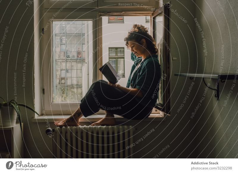 Interessierte Frau liest zu Hause am Fensterbrett lesen heimwärts Buch interessiert entspannt Literatur Fenstersims Barfuß lässig sitzen Appartement Glück