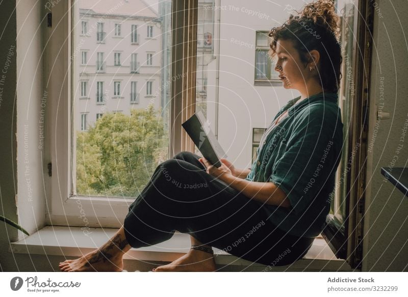 Interessierte Frau liest zu Hause am Fensterbrett lesen heimwärts Buch interessiert entspannt Literatur Fenstersims Barfuß lässig sitzen Appartement Glück