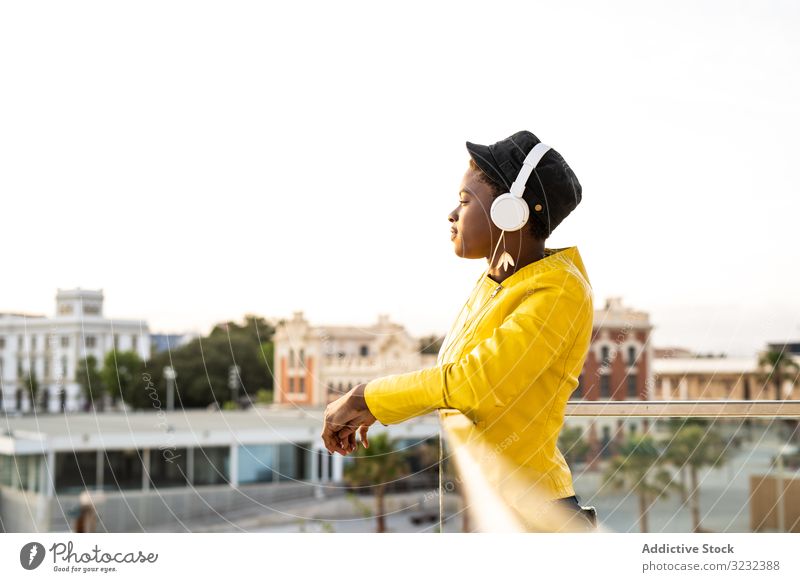 Friedliche Frau genießt Musik und entspannt sich auf dem Balkon Kopfhörer friedlich Inhalt trendy Afroamerikaner sich[Akk] entspannen fettarm Glas genießen