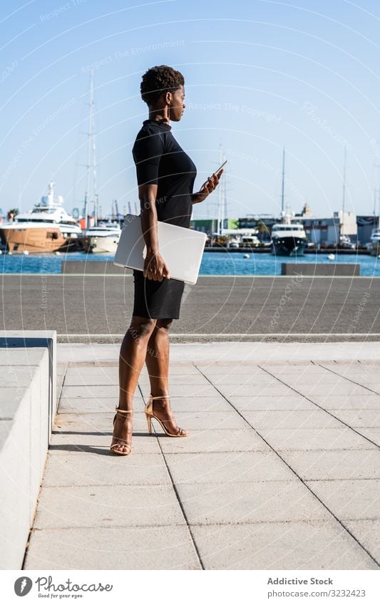 Schwarze Frau benutzt Mobiltelefon auf der Straße Laptop sich[Akk] entspannen benutzend Surfen Afroamerikaner modern elegant Kleid schwarz Gebäude Straßenbelag