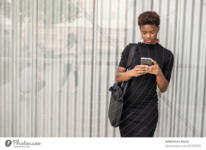 Konzentrierte weibliche Nutzung eines Mobiles in der Nähe eines städtischen Gebäudes Frau Smartphone Nachricht Straße urban benutzend Afroamerikaner fokussiert