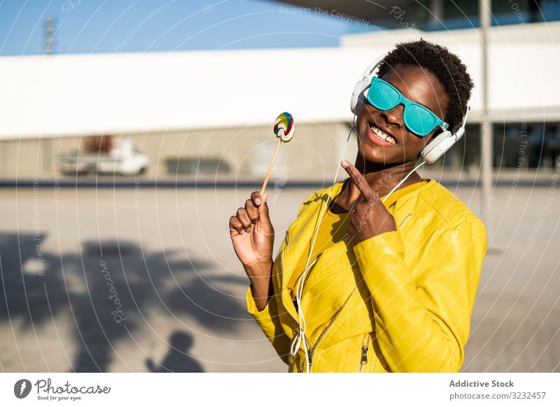 Schwarze Frau isst Süßigkeiten Lollipop cool trendy Bonbon Afroamerikaner Jacke gelb Sonnenbrille genießen süß Sommer Spaß kleben jung Mode niedlich
