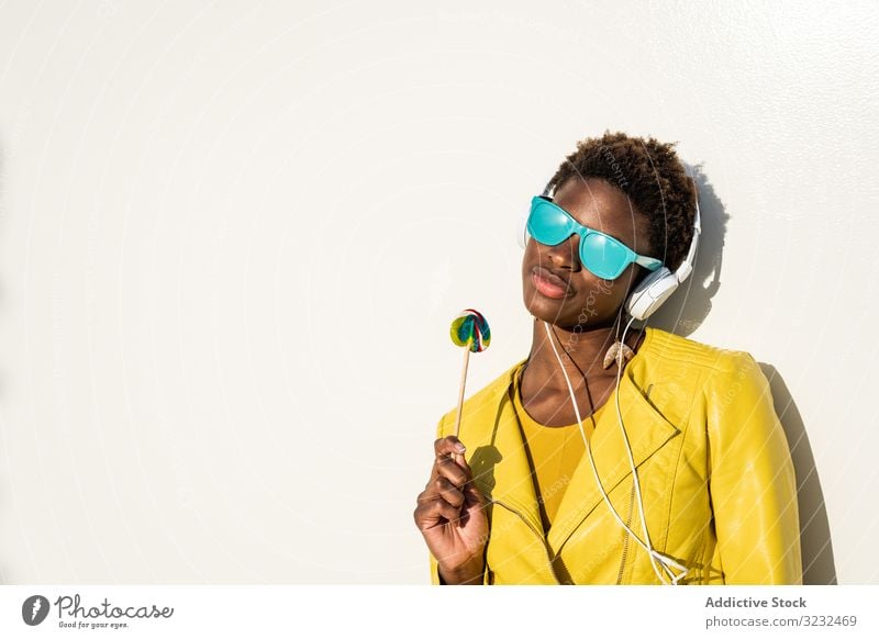 Schwarze Frau isst Süßigkeiten Lollipop cool trendy Bonbon Afroamerikaner Jacke gelb Sonnenbrille genießen süß Sommer Spaß kleben jung Mode niedlich