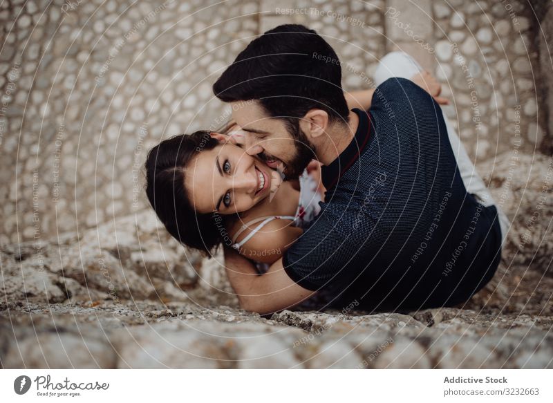 Glückliches Paar küsst sich beim Sitzen auf der Steinstraße Kuss Stadt Straße Liebe romantisch Zuneigung spielerisch lässig Umarmen kuscheln gepflastert Sommer