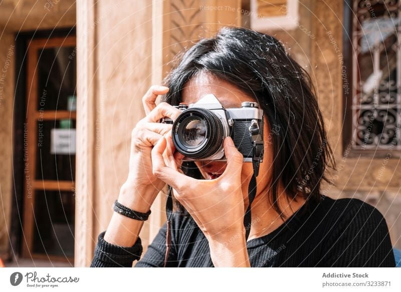 Weibliche Fotografin, die auf der Straße mit der Kamera fotografiert Fotokamera fotografierend Frau positiv Lächeln lässig Einstellung benutzend Optik sitzen