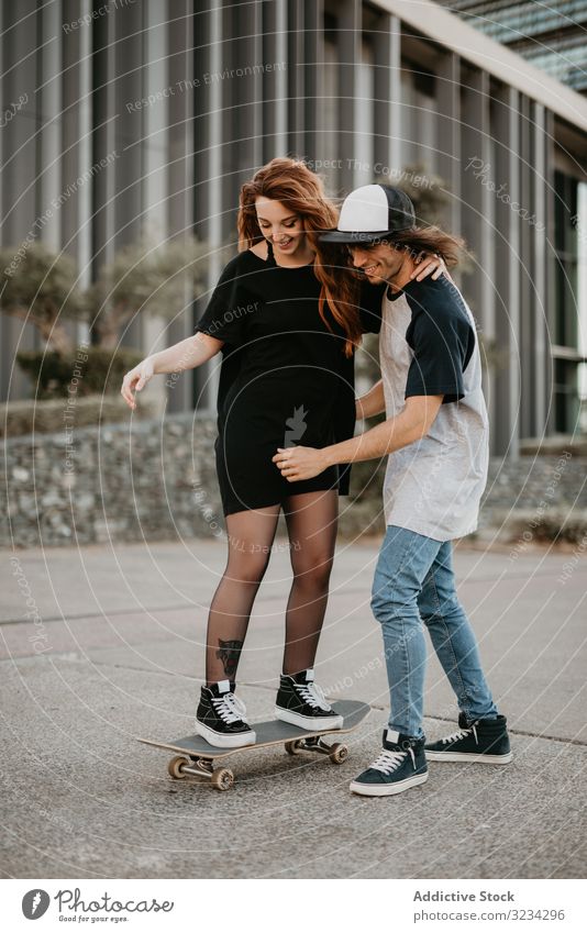 Teenager hilft seiner Freundin beim Schlittschuhlaufen auf der Straße Skateboard lernen Paar Zusammensein Spaß üben Glück abstützen Hilfsbereitschaft heiter