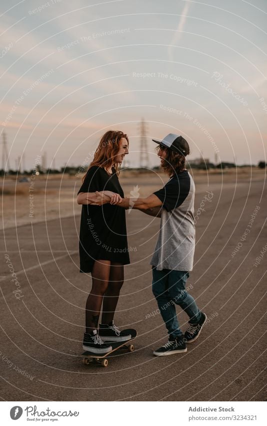 Teenager hilft seiner Freundin beim Schlittschuhlaufen auf der Straße Skateboard lernen Paar Zusammensein Spaß üben Glück abstützen Hilfsbereitschaft heiter