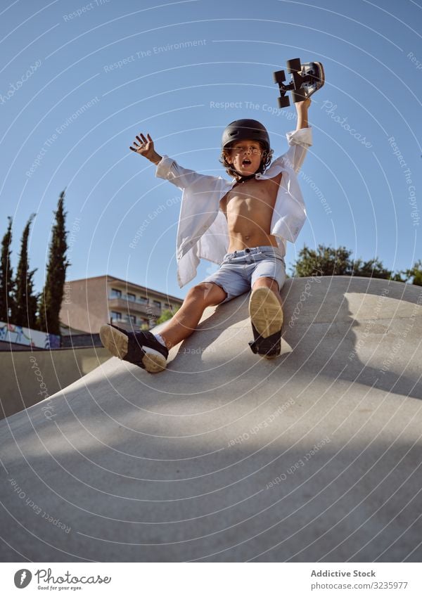 Kind auf Rampe mit Skateboard in der Hand Skatepark Mitfahrgelegenheit Spaß Schutzhelm Trick modern Blauer Himmel Schreien Sie Sport Freizeit Hobby bereit Junge