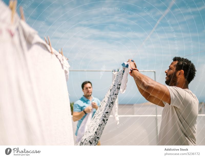 Multirassische Männer, die an hellem Tag Kleider aufhängen Haushaltsführung Wäsche waschen erhängen Kleidung Verständnis Mode Wäscherei Hausarbeit Hausaufgabe
