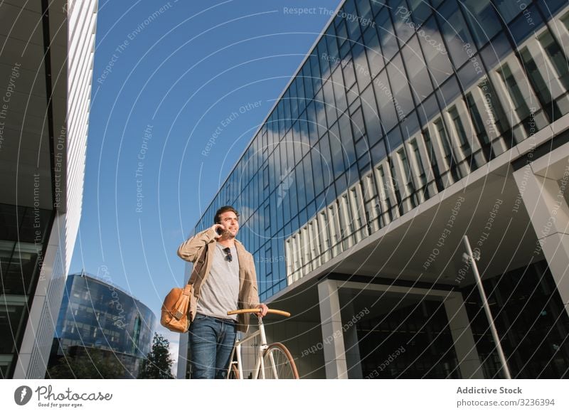 Mann telefoniert, während er vor einem modernen Gebäude in der Innenstadt steht Smartphone Handy Straße Wolkenkratzer urban reden Fahrrad besinnlich Versand
