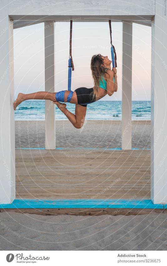 Fröhliche Frau streckt Bein auf blauer Hängematte für Luftyoga auf Holzbühne Luft-Yoga Übung Gleichgewicht akrobatisch Fitness Antigravitations-Yoga jung