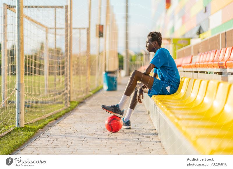 Afroamerikanischer Fussballspieler ruht sich im Stadion aus Teenager Fußball Feld sitzen Sitz Pause Ball Training Sportbekleidung ethnisch männlich Jugendlicher