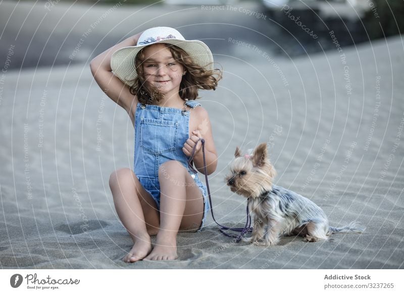 Süßes Mädchen mit Hut in der Hand und mit Hund am Strand sitzend Haustier Sand Sommer MEER Tier Freundschaft Begleiter Urlaub Spaß Ufer Natur windig
