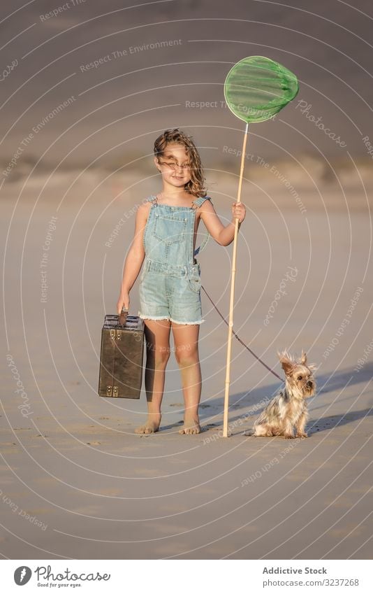 Neugieriges Kind mit Koffer und Schmetterlingsnetz auf Sand stehend mit Hund Mädchen Sommer MEER Tier Freundschaft Haustier Begleiter Urlaub Spaß Ufer Strand
