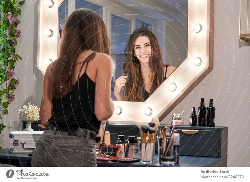Lächelnde Frau betrachtet Spiegel in der Hand im Kosmetiksalon Reflexion & Spiegelung Salon Make-up Pflege Behandlung Gerät Stil bequem Schönheit Innenbereich