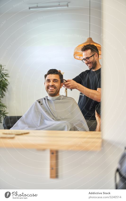 Spiegelung im Spiegel eines Klienten, der lacht, während der Friseur ihm die Haare mit einem Rasiermesser schneidet Dienst Fröhlichkeit Lächeln Hände Reflexion