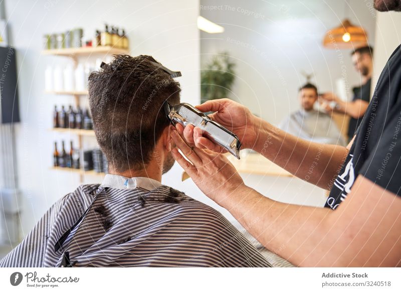 Rücken eines Kunden in einem Friseurladen, der auf einem Stuhl sitzt und sich die Haare schneidet Dienst Hände Spiegel Reflexion Rasierapparat geschnitten