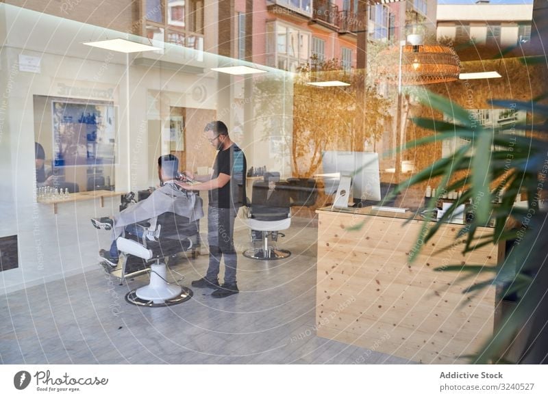 Ansicht eines Friseursalons von außen mit einem Friseur im Inneren, der einem Kunden die Haare schneidet Design Reflexion Fenster Ladenfront Straße