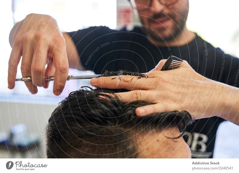 Detail einer Hand von einem Friseur, der einem Kunden mit Schere und Kamm die Haare schneidet, mit der Unschärfe im Hintergrund geschnitten Haarschnitt Salon
