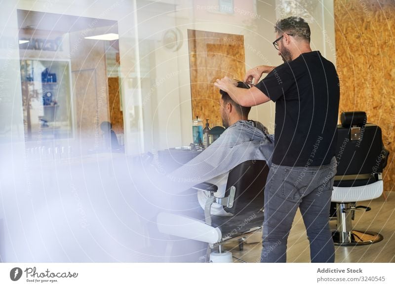 Ansicht eines Friseurladens von außen durch beschlagenes Glas mit einem Friseur im Inneren, der einem Kunden die Haare schneidet vertikal Reflexion Fenster