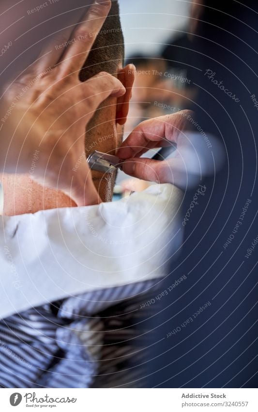 Vertikales Foto eines Ausschnitts der Hände eines Friseurs, der einem Kunden mit einem Rasiermesser die Haare schneidet vertikal Rasierer handgefertigt