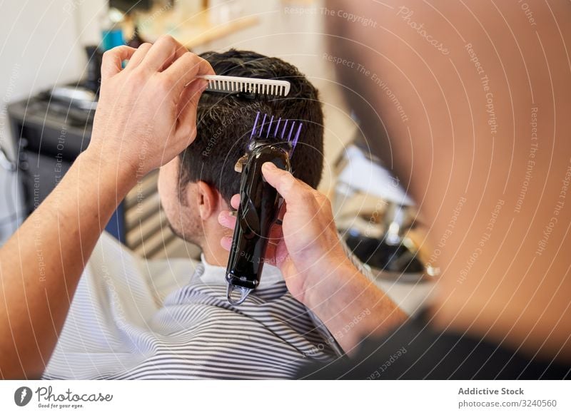 Friseur, der einem Kunden, der auf dem Friseurstuhl sitzt, mit einer Maschine Haare schneidet Rasierapparat geschnitten Barbershop Kamm Frisur Möbel Arbeit