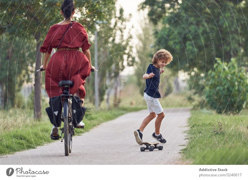 Mutter und Sohn reiten entlang des Parkwegs Mitfahrgelegenheit Weg Skateboard Fahrrad Zusammensein Spaß Familie Glück Junge Frau Kind Sommer Freude froh