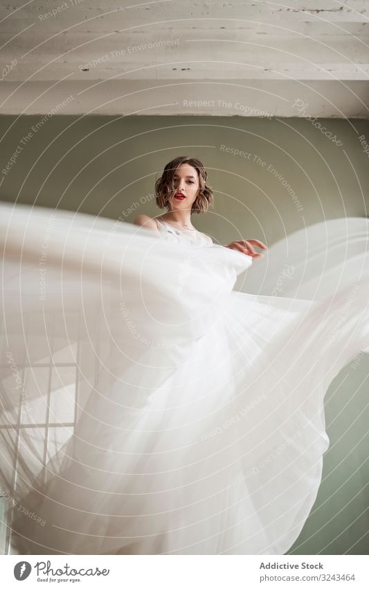 Attraktive, heitere junge Frau in weißem Kleid tanzt und schaut in die Kamera Brautkleid fließen Angebot durchsichtig schlanke sanft rote Lippen